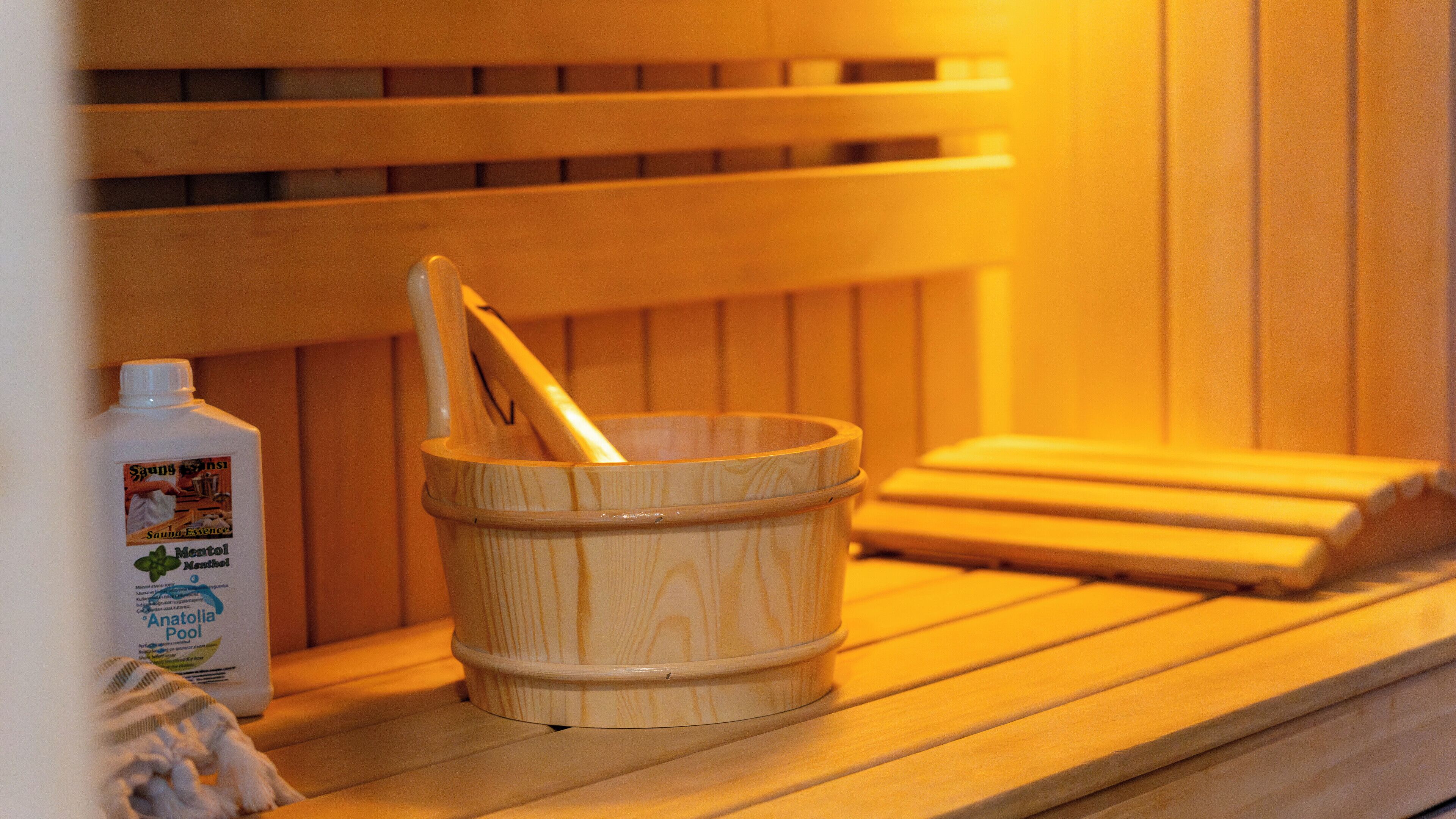 A wooden sauna bench with a wooden bucket containing a wooden mallet.