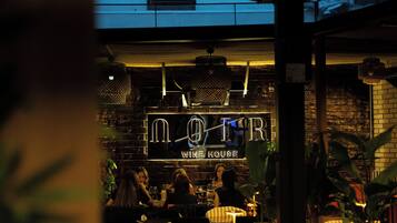 A wine house interior with a brick wall, hanging lights, and a group of people seated at tables.