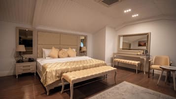 A bedroom with a large bed, a bench, a chair, a desk, and a mirror.