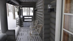 A log cabin with a wooden porch, metal chairs, and a window with a view of snow-covered trees. - Cottage H62 Ruokolahti (Ruokolahti)