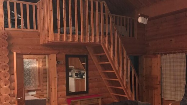 A log cabin interior with a loft bedroom, a dining area, and a living room with a sofa and a coffee table. - Cottage H62 Ruokolahti (Ruokolahti)