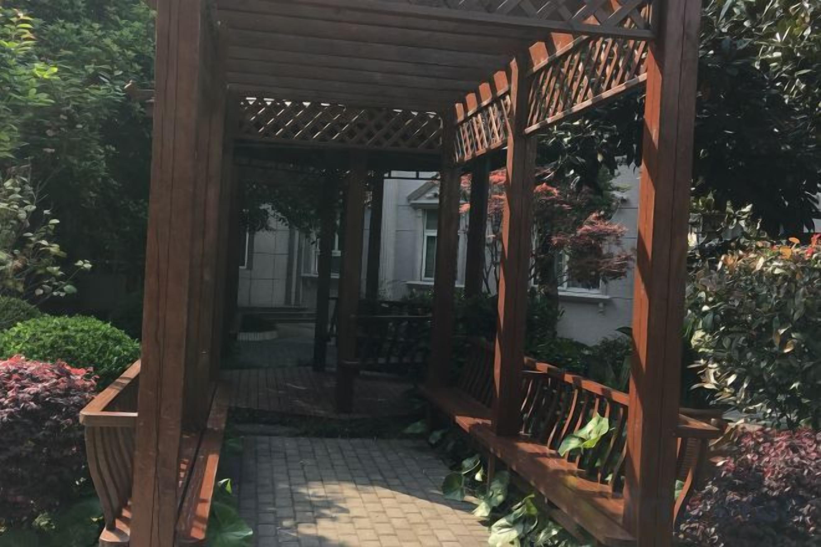 A wooden pergola structure with a brick pathway leading to a seating area.