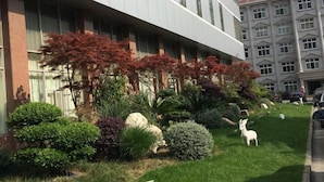 A modern building with a well-maintained garden featuring various shrubs and a decorative white goat statue. - Jinxiu Hotel (Shanghai)