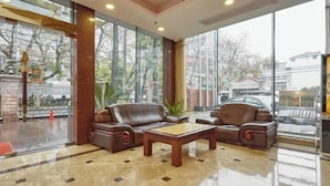 A lobby with leather sofas, a wooden coffee table, and large windows offering a view of the outside. - Jinxiu Hotel (Shanghai)
