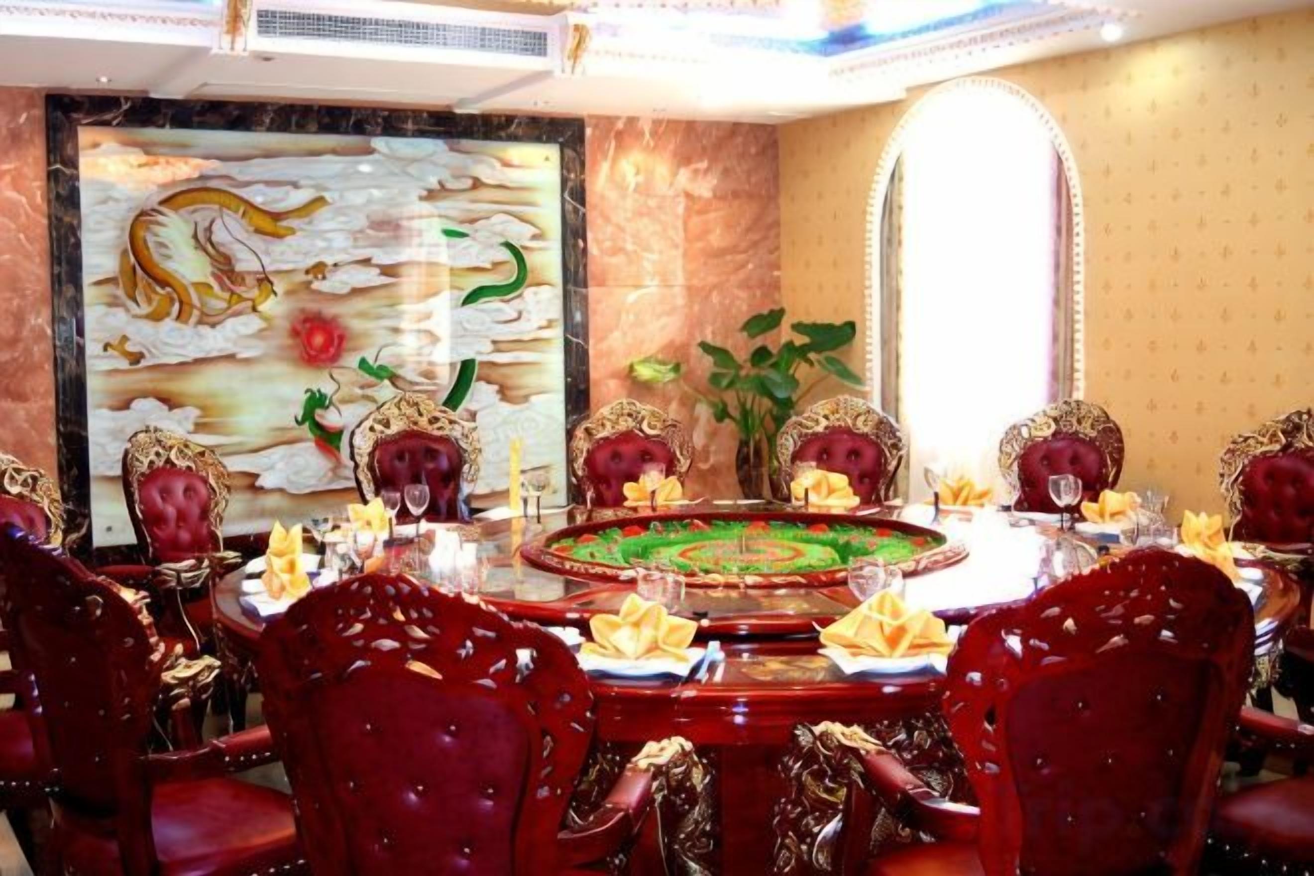 Uma sala de jantar com uma mesa redonda, cadeiras estofadas em vermelho e um grande quadro decorativo na parede.