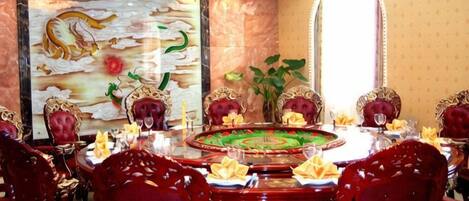 Een eethoek met een ronde tafel, rode bekleden stoelen en een groot decoratief schilderij aan de muur.