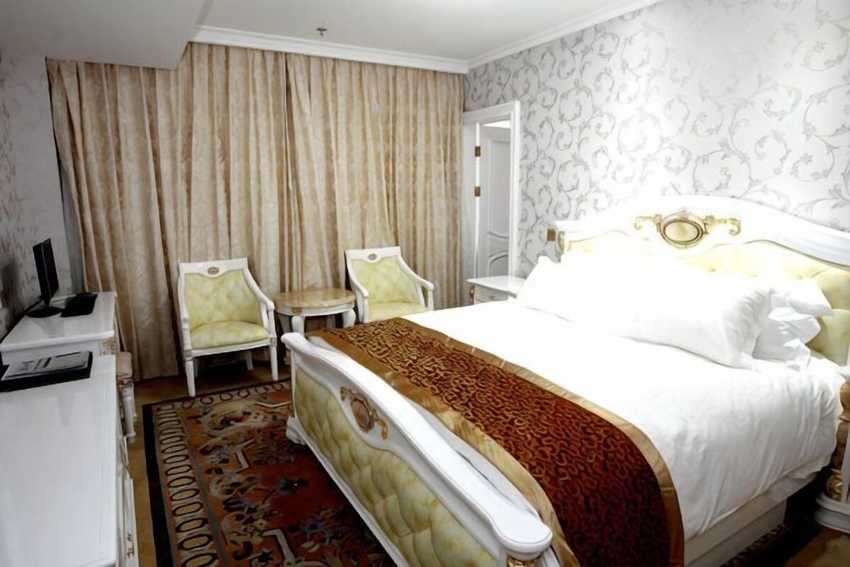 A hotel room with a bed, two chairs, a desk, and a television.