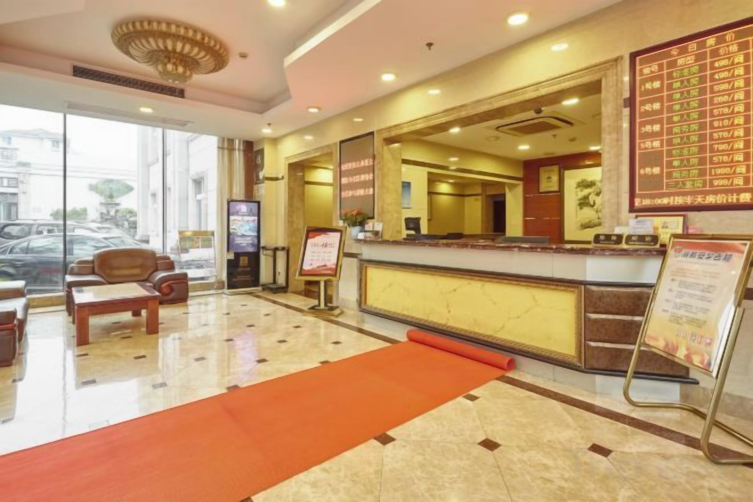 A hotel reception area with a marble floor, a reception desk, a red carpet, and a digital screen.