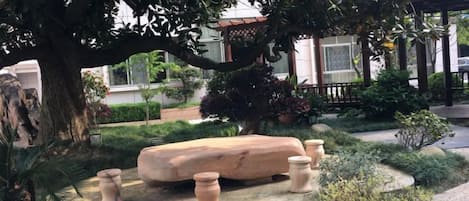 Ein Garten mit einer Steinsitzbank, Blumentöpfen und einem Pavillon.