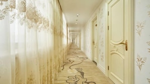 A long, narrow hallway with ornate wallpaper and patterned carpet. - Jinxiu Hotel (Shanghai)