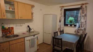 Une cuisine de taille réduite avec des meubles en bois, un réfrigérateur blanc, une table à manger avec des chaises et une fenêtre avec des rideaux.