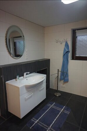 A bathroom with a white sink, dark tiled walls, a mirror, and a blue towel rack. - Schmidtappartement (Berlin)