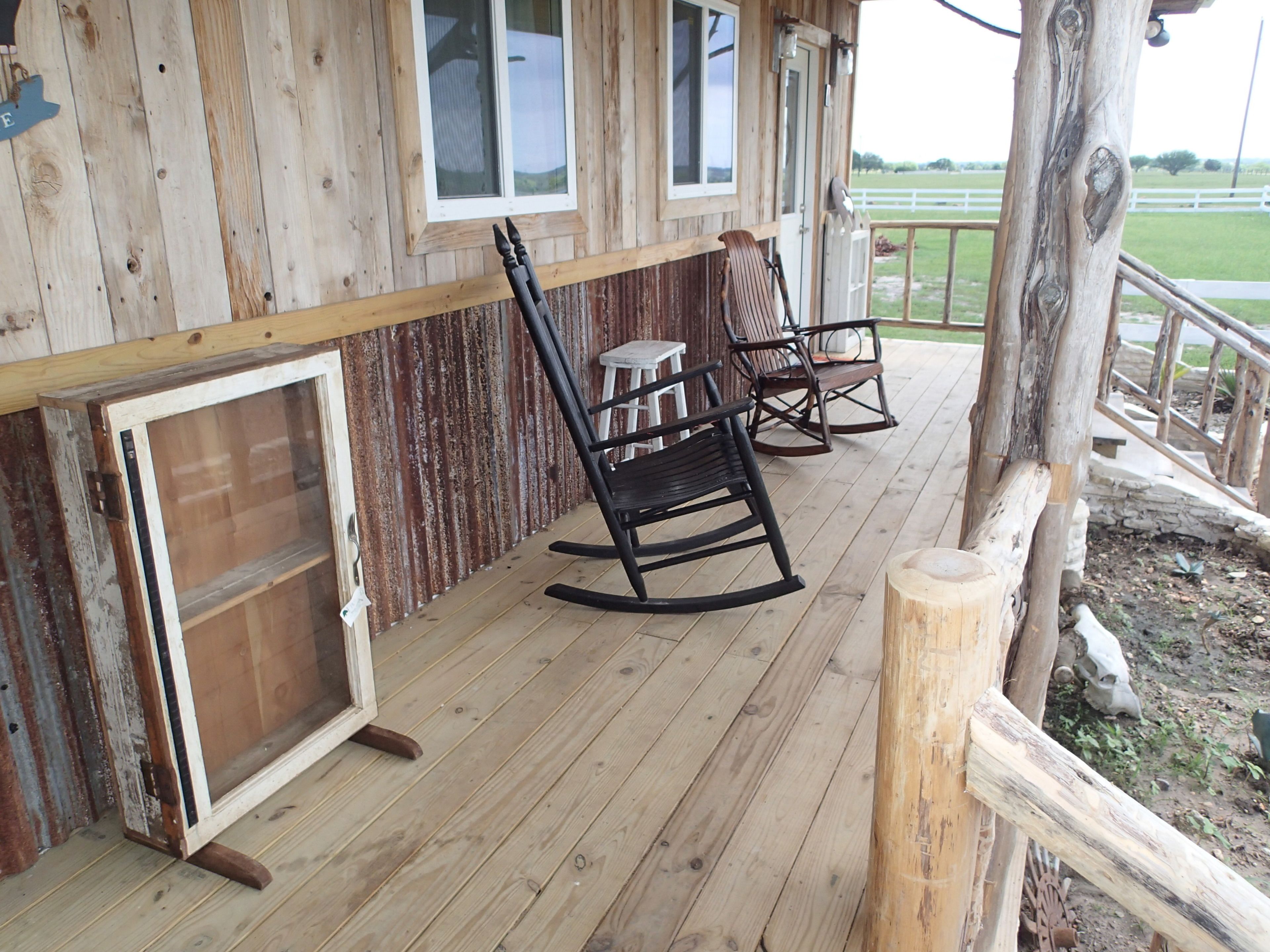 A wooden porch with rocking chairs and a table, overlooking a grassy field.