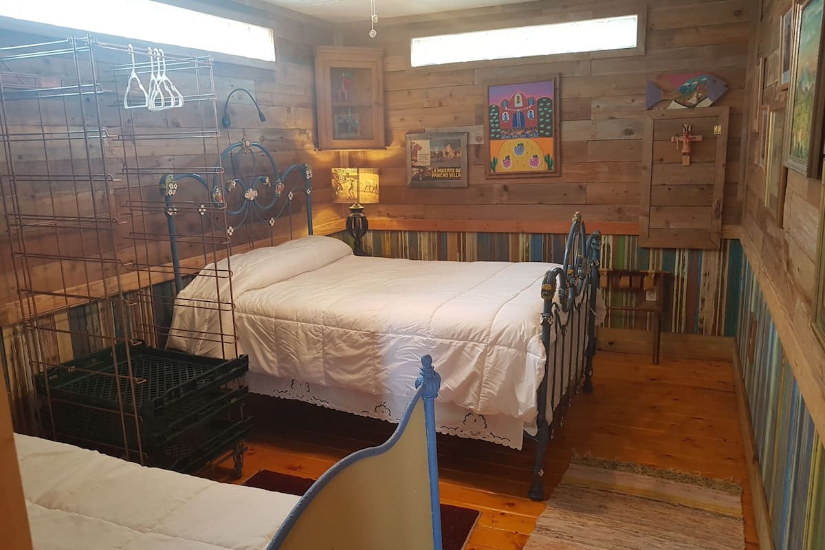 A rustic wooden room with a bed, a small table, and a wall-mounted rack.