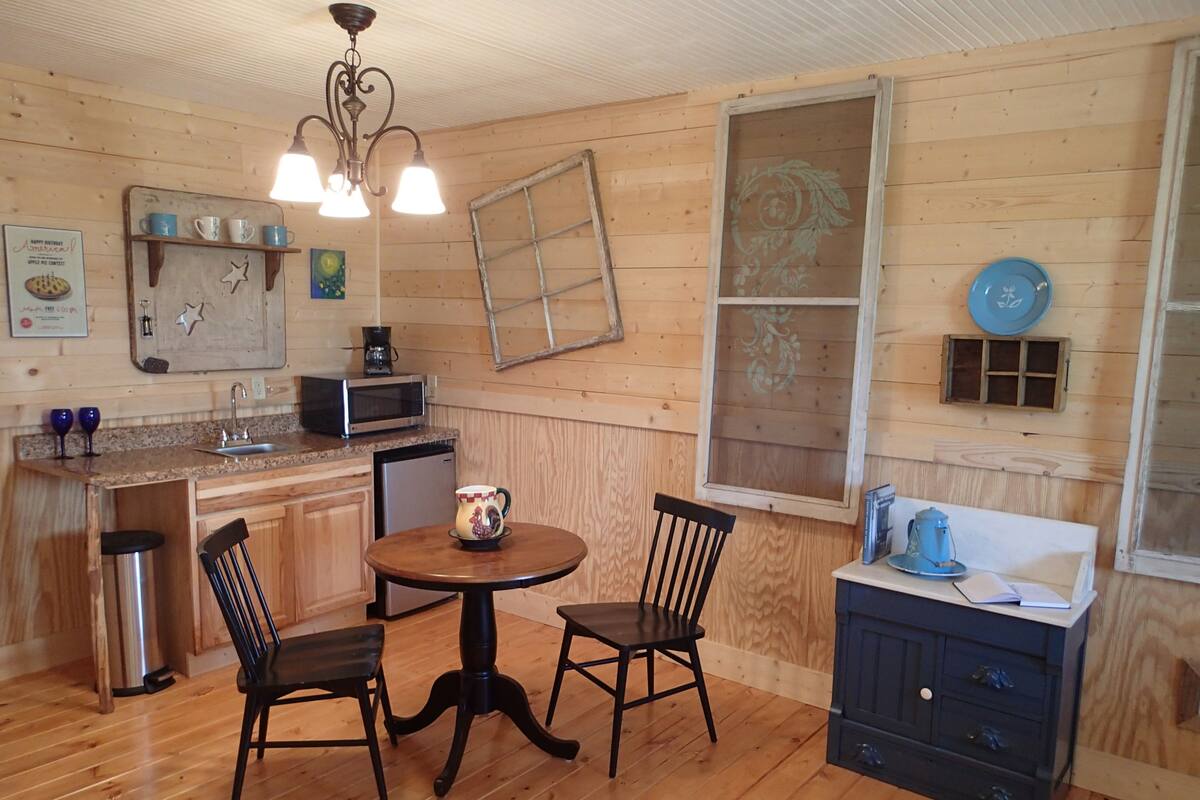 A cozy kitchen with wooden walls, a dining table with chairs, a microwave, and a coffee maker.