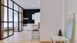Ein modernes Hotelzimmer mit einer großen Schiebeglasdoor zum Balkon, einer Küchenzeile, einem kleinen Esstisch und einem Sessel.