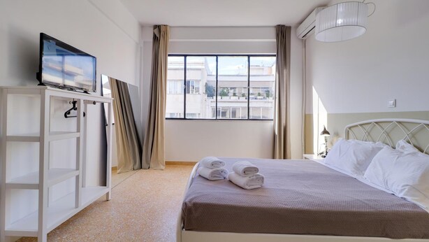 Ein Hotelzimmer mit einem Bett, einem Fernseher auf einer weißen Kommode, einem Fenster mit Vorhängen und einem Deckenventilator.