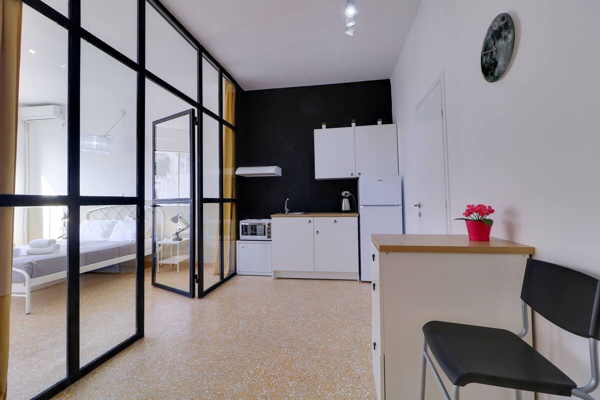 A modern room with a bed, kitchenette, and a chair.