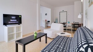 Ein modernes Wohnzimmer mit Fernseher, weißem Sofa, niedrigem schwarzen Couchtisch und einem gemusterten Sofa.