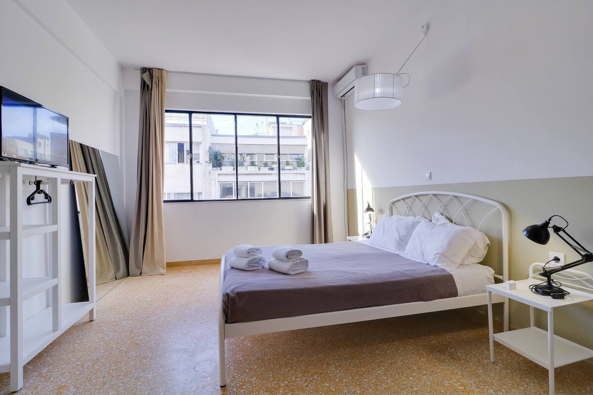A hotel room with a bed, a desk, a TV, and a window with curtains.