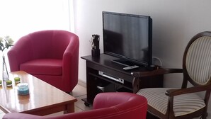 Un salón con una televisión de pantalla plana, un sofá rojo, una silla a rayas y una mesa de centro de madera.