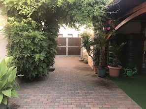A brick pathway leading to a gated entrance, surrounded by lush greenery and potted plants. - Pension Borna (Borna)