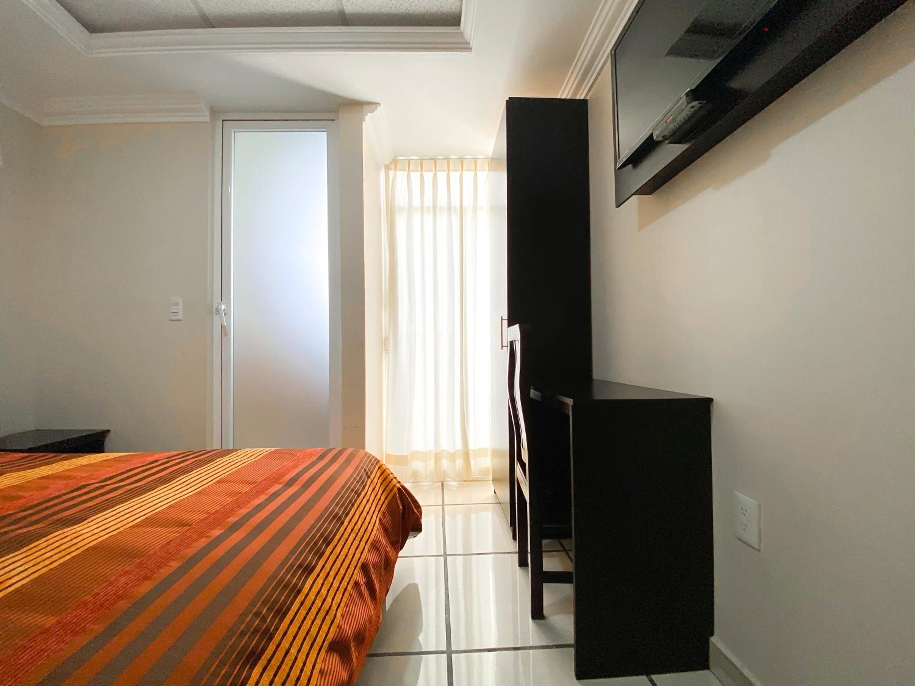 Een hotelkamer met een bed, een bureau en een aan de muur bevestigde televisie.