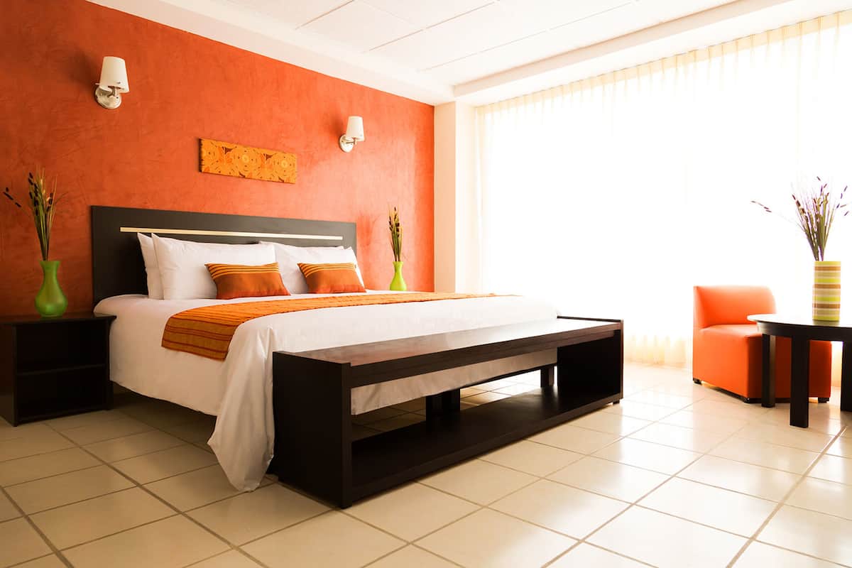 A modern hotel room with a large bed, two bedside tables, a nightstand, a small table, and a chair.