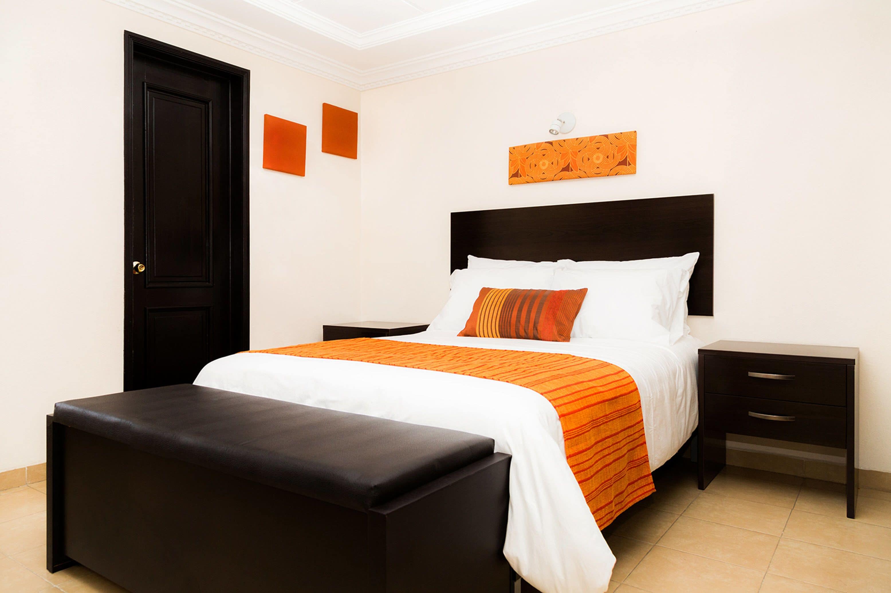 Un dormitorio ordenado con una cama, una mesita de noche y un banco.