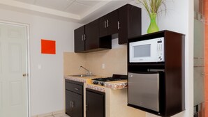 Une cuisine de taille réduite, dotée de meubles de rangement sombres, d’un four à micro-ondes, d’une cuisinière et d’un réfrigérateur.