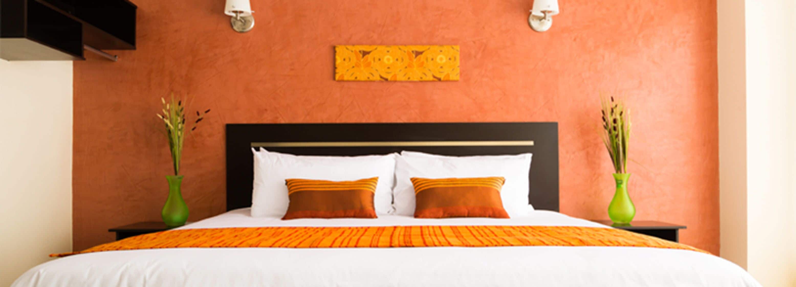 A hotel room with a large bed, two vases of plants, and a decorative wall piece.