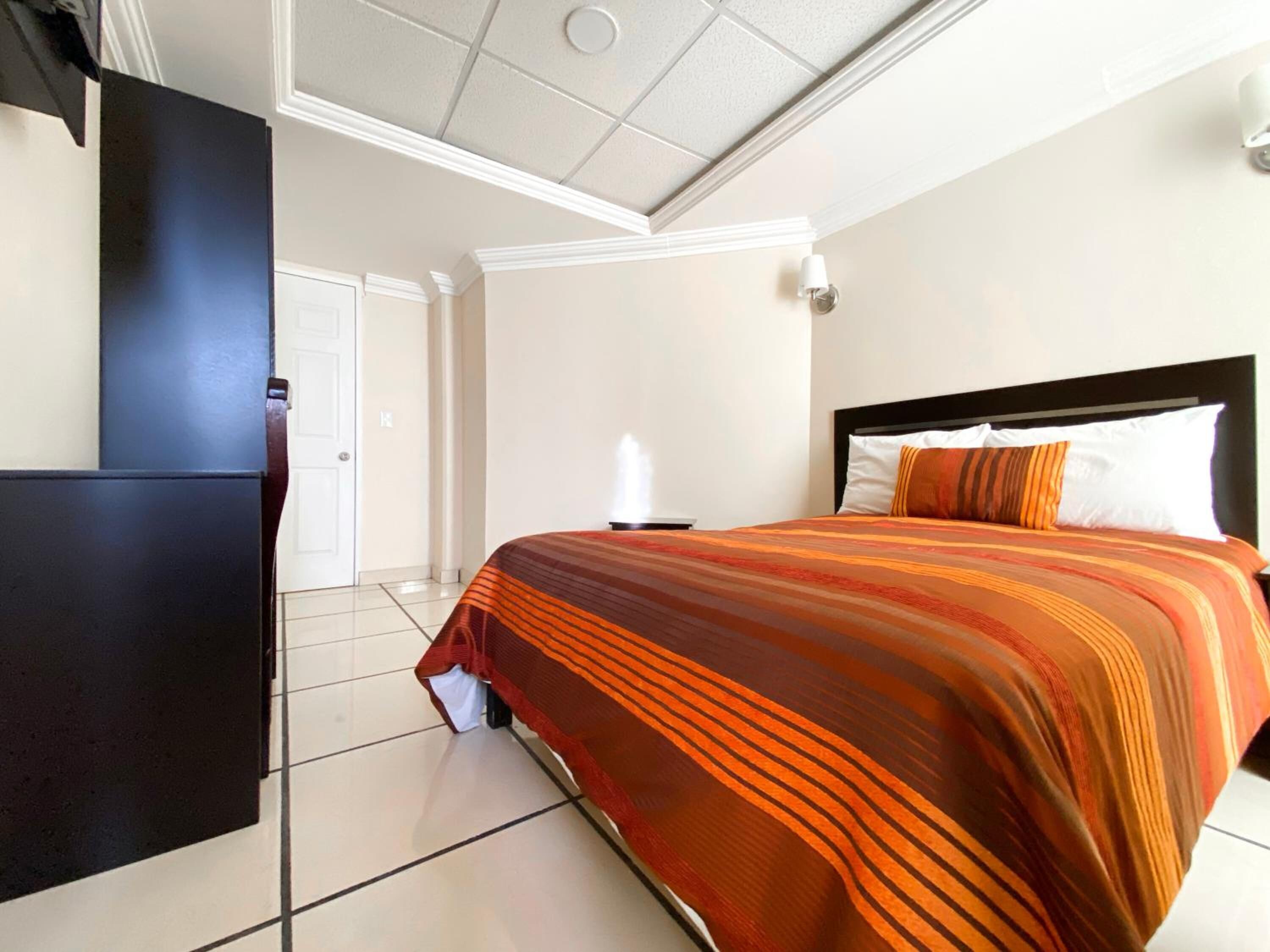 A hotel room with a bed, a black wardrobe, a white door, and a tiled floor.