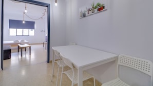A modern, minimalist room with a white table and chairs, a small shelf with plants, and a view into another room with a bed and a window. - athens.apartotel.2 (Athens)