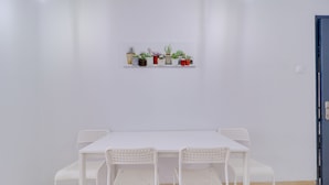A white table with four chairs, a white wall, and a shelf with potted plants. - athens.apartotel.2 (Athens)
