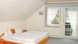 A bedroom with a wooden bed, white bedding, a nightstand, a lamp, and a window with curtains. - Gasthof Zum Dorfkrug (Winterberg)
