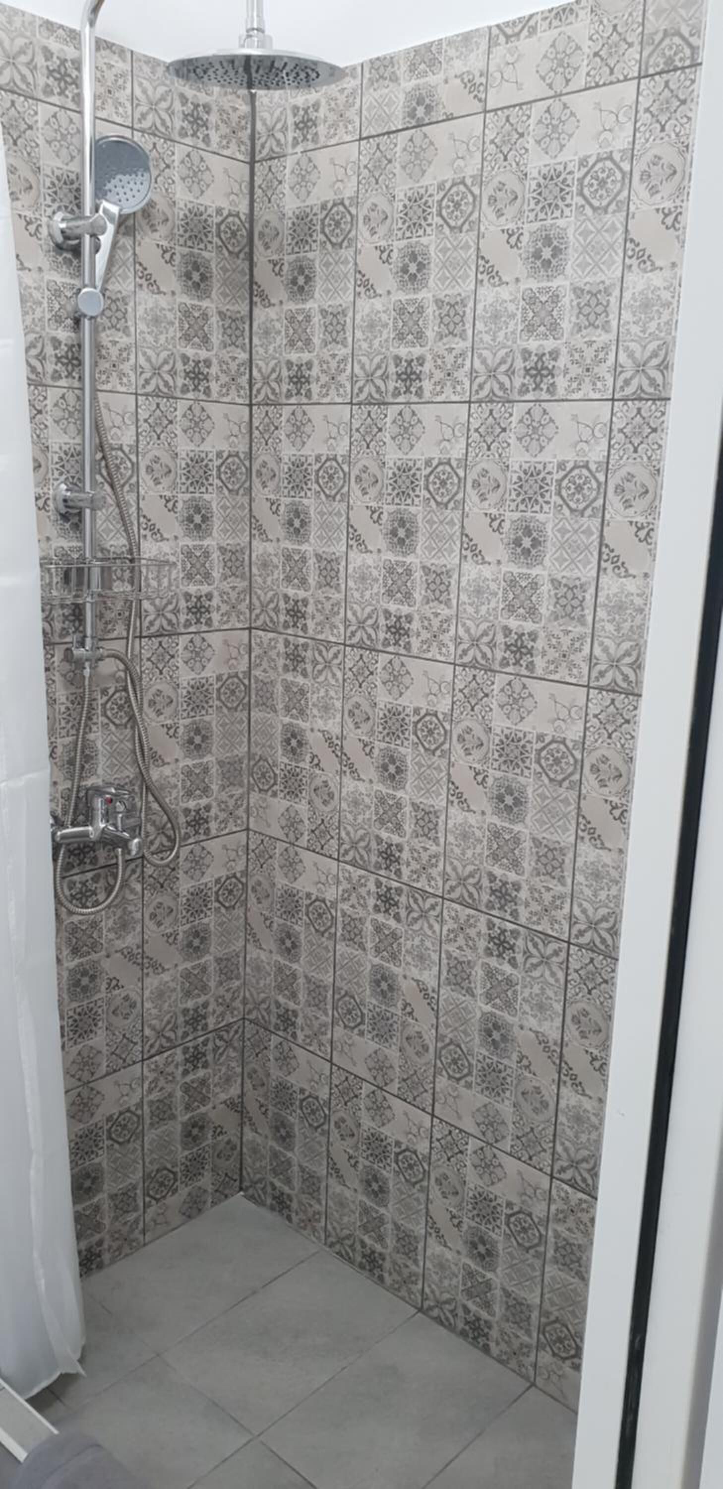 A shower with a handheld showerhead and a wall-mounted faucet. The shower area has patterned tiles.