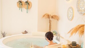 Una mujer se relaja en una bañera con una copa de vino y fruta en una bandeja.