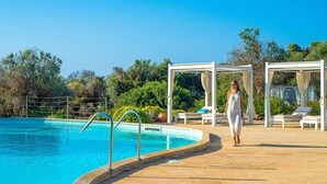 Zona junto a la piscina con una piscina azul cristalina, un sendero peatonal, sillas de descanso y una pérgola.