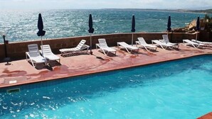 Un espace aménagé au bord de la piscine, avec des chaises longues et des parasols, donnant sur une étendue d’eau.