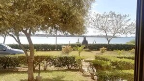 Une vue à travers une arche donnant sur un jardin aménagé, avec des arbres et une étendue d’eau en arrière-plan.