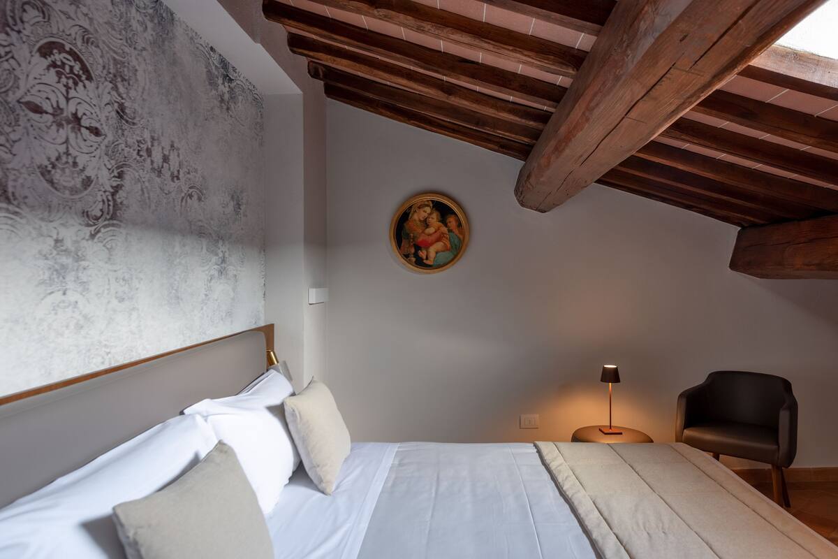 A bedroom with a bed, a chair, a lamp, and a wall with a painting.