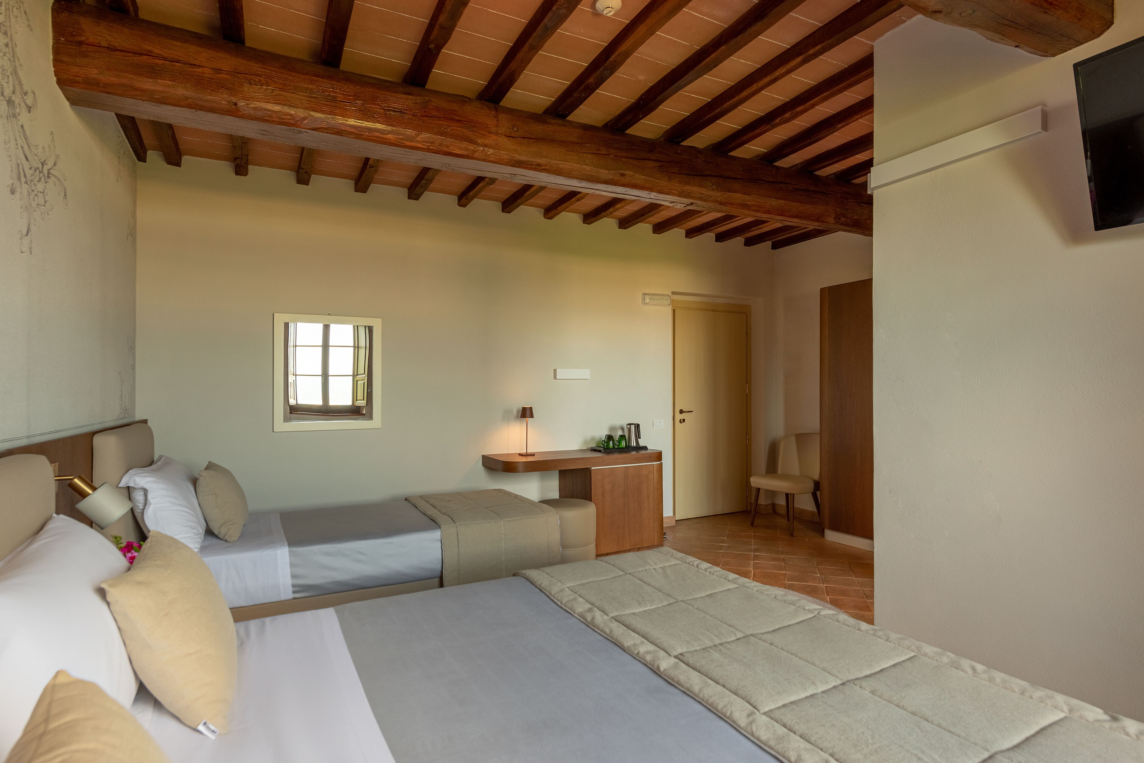 Un dormitorio con dos camas, techo de madera, un escritorio pequeño, una silla y una ventana.