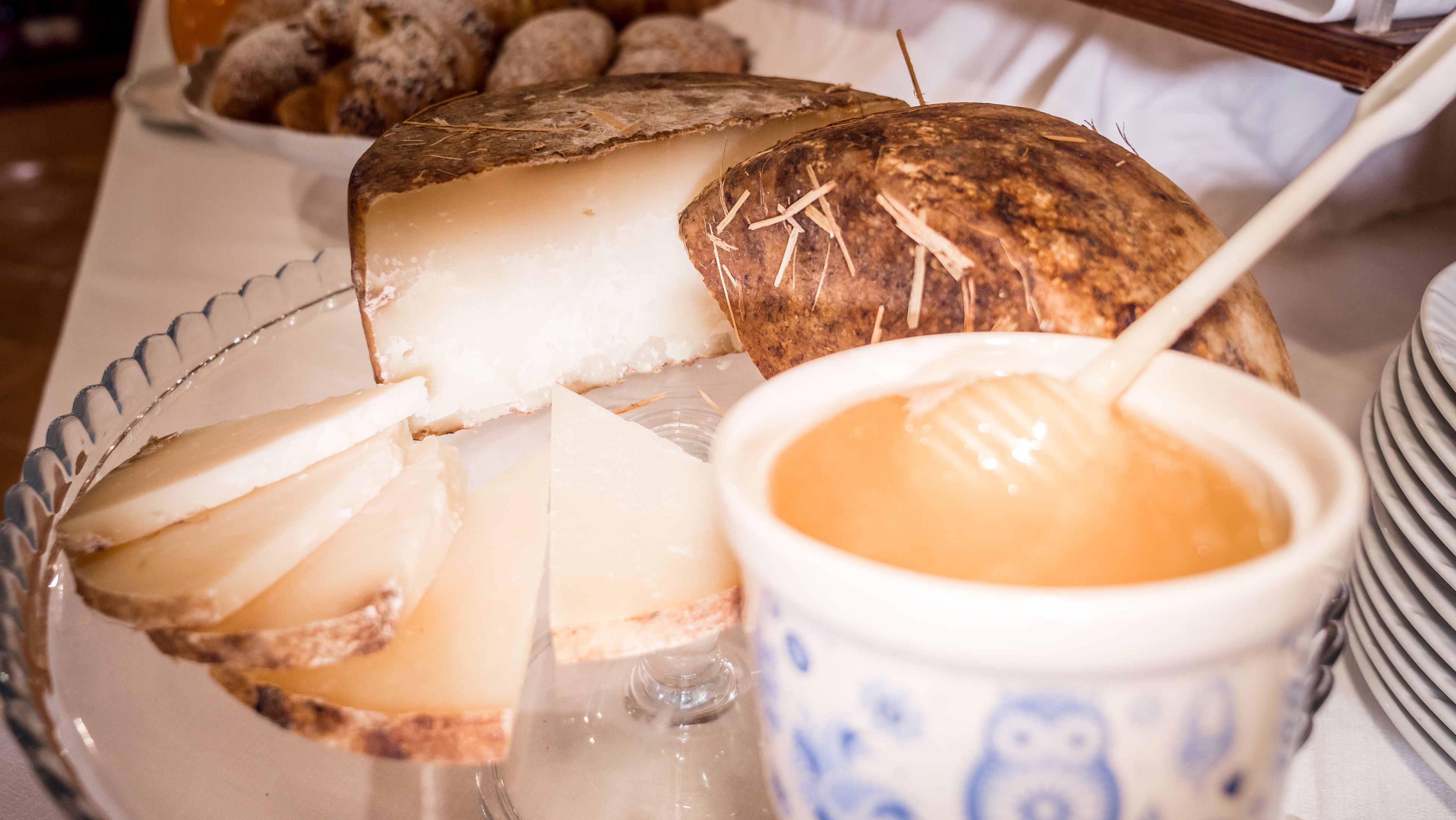 A glass bowl with a spoon, a coconut, and a loaf of bread on a table.