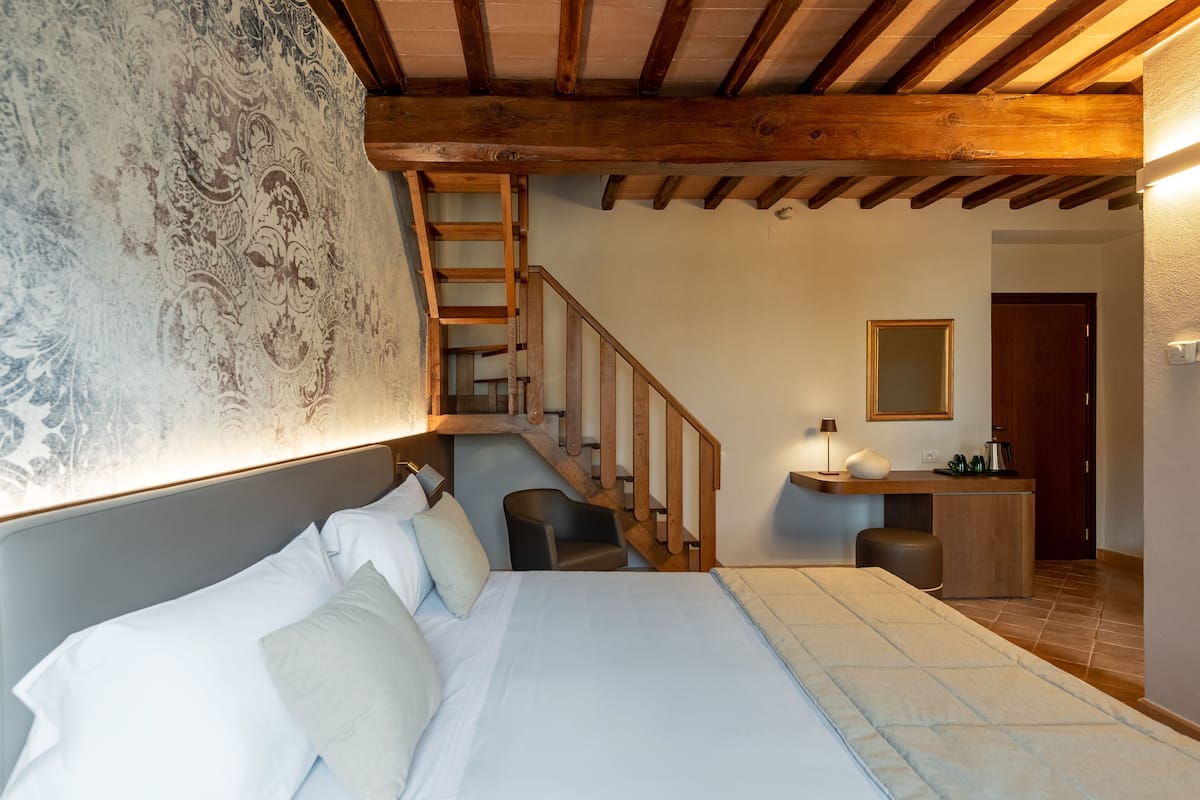 A bedroom with a bed, a desk, a chair, a staircase, and a mirror.