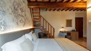A bedroom with a bed, a desk, a chair, a staircase, and a mirror.