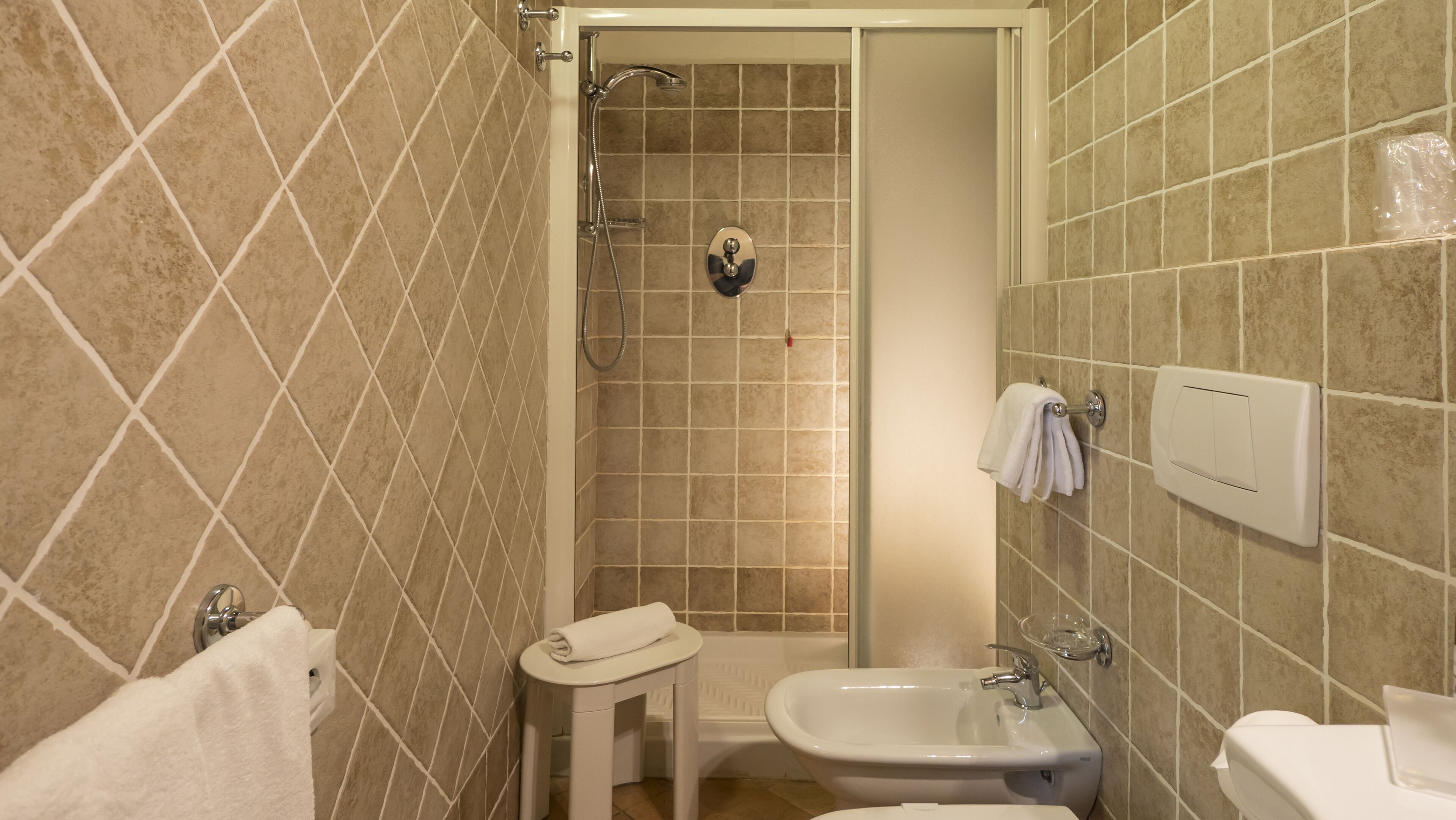 Ein Badezimmer mit beige farbenen Fliesen, einer Dusche, einem Waschbecken und einer Toilette.