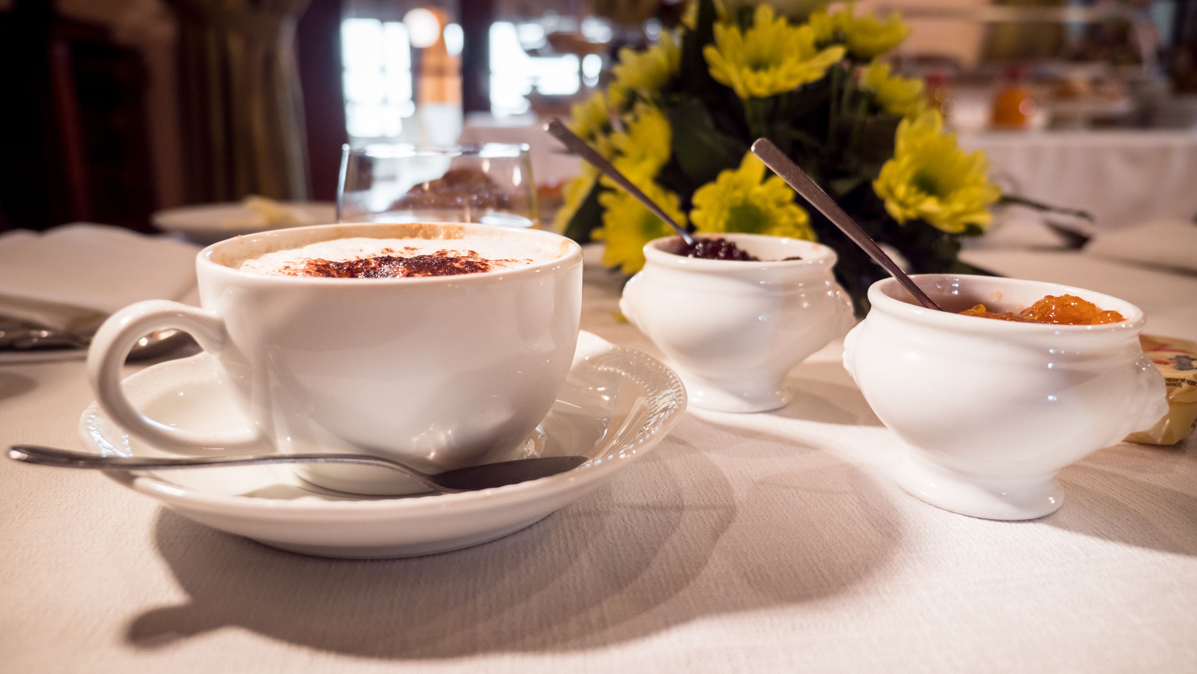 A table setting with a cup of coffee, a small bowl of jam, and a spoon.