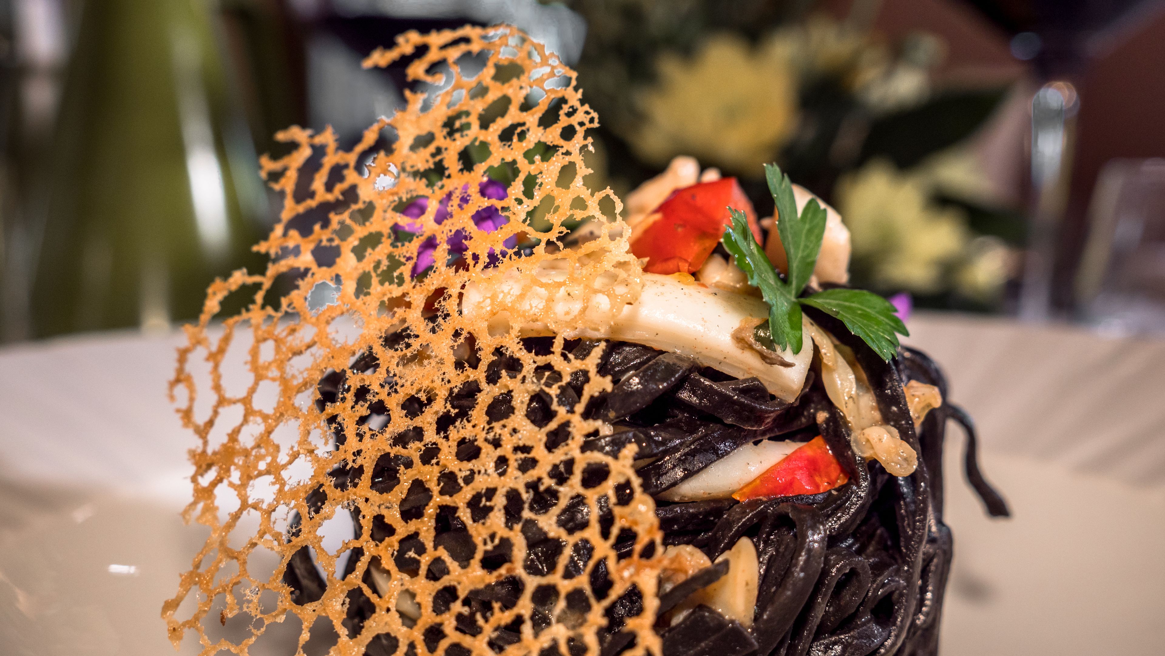 Une vue rapprochée d’un plat composé de nouilles noires, de légumes et d’un filet décoratif orange.