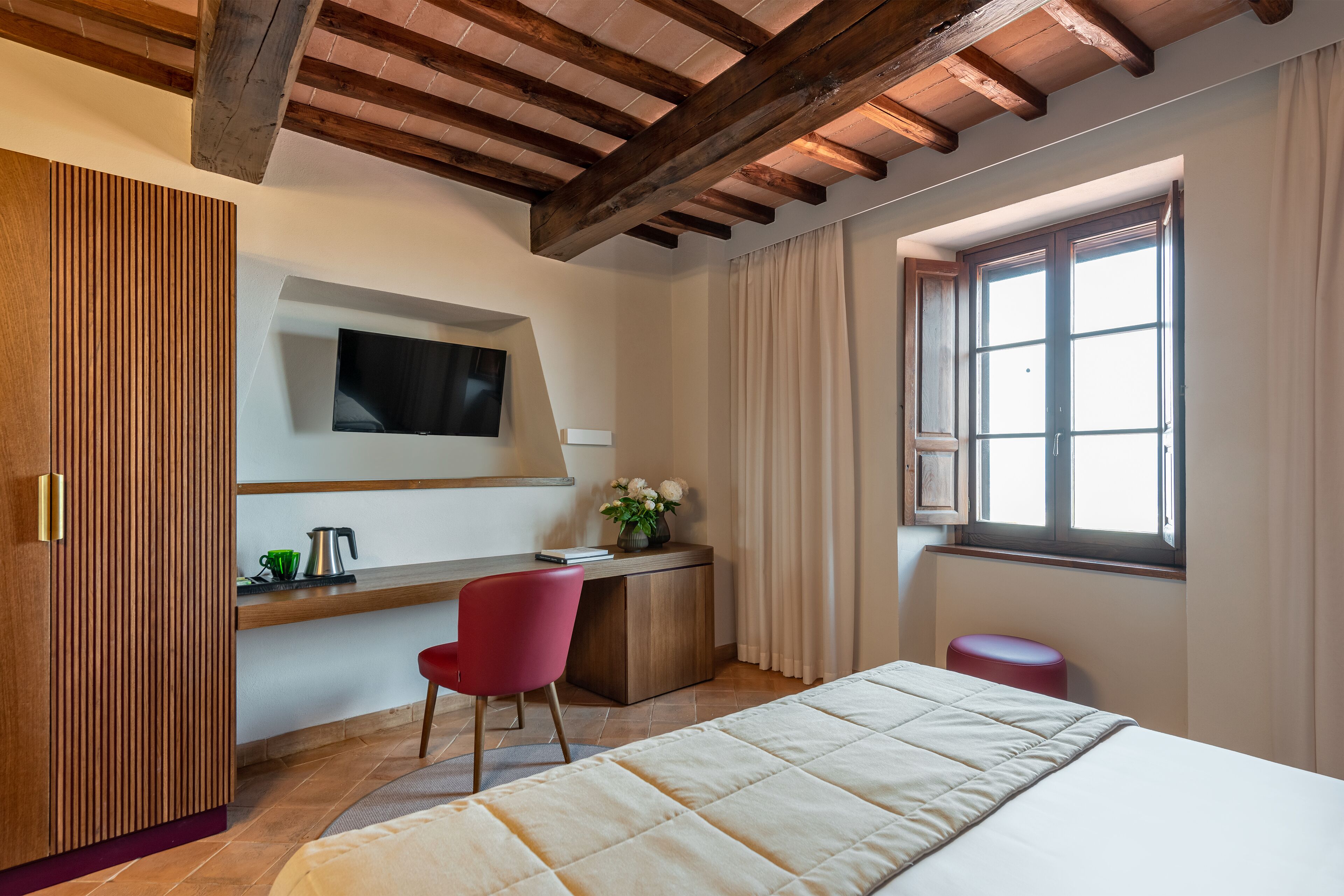 Un dormitorio con cama, escritorio con silla, televisor montado en la pared y ventana con cortinas.