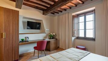 Un dormitorio con cama, escritorio con silla, televisor montado en la pared y ventana con cortinas.